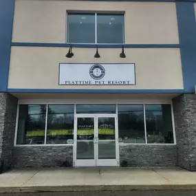 Front view of the Playtime Pet Resort Windham facility, with modern stonework, large windows, and clearly visible signage above the entrance.