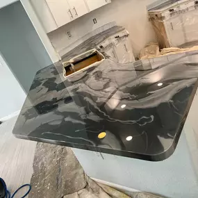 A newly installed epoxy countertop with a swirling gray and black marble-like pattern reflects light in a partially renovated kitchen.