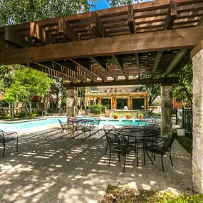 A patio with a table and chairs is shaded by a pergola