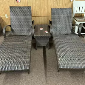 Woven rattan-style outdoor chaise lounge set with side table, perfect for relaxing in the sun.