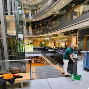 In einem modernen Einkaufszentrum in Düsseldorf reinigt ein Facharbeiter die Rolltreppe gründlich. Durch hohe Hygieneanforderungen wird eine saubere und sichere Umgebung für Besucher gewährleistet.