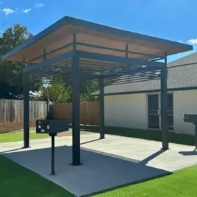 a pergola with two barbecue pits in a backyard