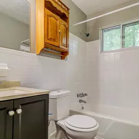 A white toilet sits in a bathroom with a white tub and a window.