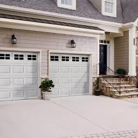 Two white Clopay Classic Collection insulated garage doors with windows are attached to a house with tan siding and a stone facade.