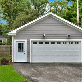 A white garage door with windows is attached to a gray, one-car garage with a white door on the side.