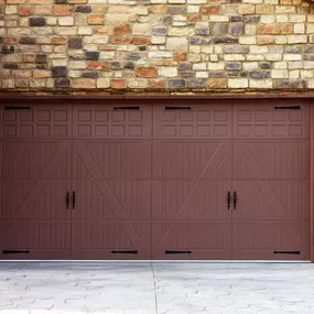 The image shows a brown Ammar carriage garage door with decorative black hardware, set in a stone-clad garage.