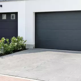 A modern, dark gray garage door is shown next to a smaller, dark gray door with three small windows, set in a white building.