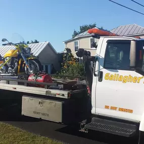 A yellow motorcycle is secured on the flatbed of a white 