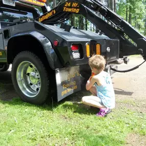 A young child is squatting near the rear of a black Gallagher's Towing truck, with visible text and markings.