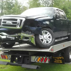 A damaged black Ford truck is loaded onto the flatbed of a red Gallagher's Towing truck on a roadside.