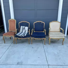 Four French Provincial walnut upholstered lounge chairs with varying fabric patterns are arranged in front of a gray garage door.