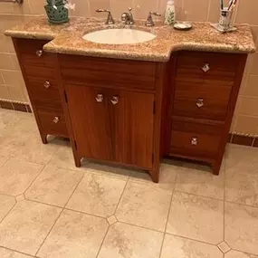 A wooden bathroom vanity with a granite countertop and a sink is shown in a bathroom with tiled walls and flooring.