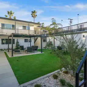 A patio with a table and chairs is surrounded by a green lawn.