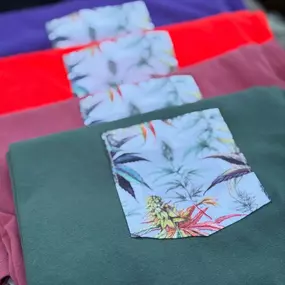 Stack of colorful folded shirts with tropical patterned pockets, available at The Agriculturalist Dispensary
