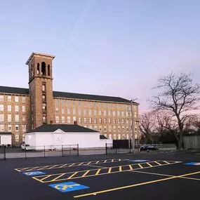 Wide view of The Agriculturalist cannabis dispensary and its accessible parking lot in Fall River, set against a historic building.