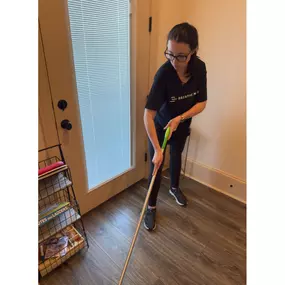 This image captures a Breathe Maids cleaning professional hard at work, ensuring a spotless and well-maintained home. She is wearing a Breathe Maids branded black t-shirt, reinforcing the company’s professional and polished look. Focused and detail-oriented, she is mopping the hardwood floor near a bright entryway, demonstrating the company’s commitment to thorough, high-quality cleaning services.

The cozy home setting, with neatly organized storage shelves and a welcoming atmosphere, highlight
