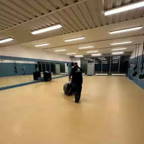 Ein weitläufiger, leerer Raum mit Spiegelwand und Turngeräten wird professionell mit einer Reinigungsmaschine gesäubert.