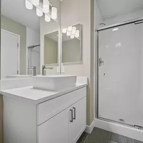 A white bathroom with a sink, mirror, and shower.