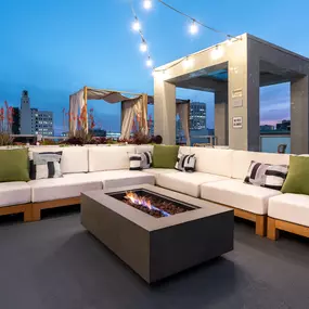 Sunset rooftop deck at Riva Apartments in Santa Monica, CA, featuring a cozy fire pit and plush lounge seating with panoramic city views.