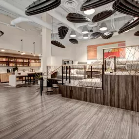 Modern communal workspace at Harlow Apartments featuring a mix of seating areas, including a sunken lounge with built-in cushions, a central table with chairs, and a kitchenette with bar stools.