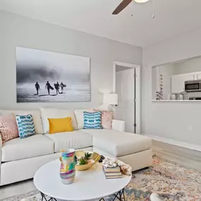 A living room with a white couch and a painting of three people walking on a beach