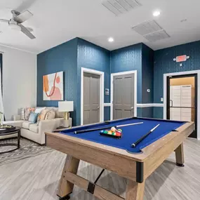 A pool table is in the middle of a room with a couch and a fan