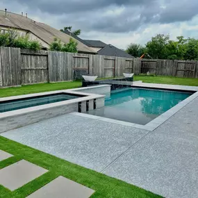 Pool, raised spa, scuppers, concrete deck, turf with stone pavers, retaining wall with fountains