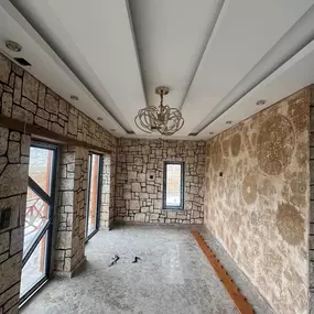 This room transformation includes faux-stone paneling, textured art walls, and layered ceiling beams—reflecting a classic-meets-contemporary vibe, ideal for lounges or sunrooms.