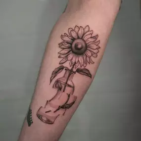 Illustratives Fineline/Linework Tattoo einer Sonnenblume in einer abstrakten Vase.