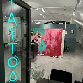 Empfangs- und Wartebereich im OMEN Tattoo Studio Berlin Mitte mit Galerie-Flair, heller Einrichtung und stilvollem Neon-Schriftzug.