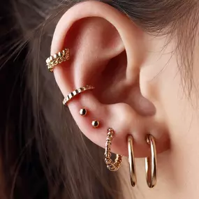 Detailaufnahme eines Ohrs mit mehreren goldenen Piercings in unterschiedlichen Formen und Positionen.