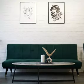 Wartebereich im OMEN Tattoo Studio Berlin Mitte mit Galerie-Flair, heller Einrichtung und freiliegenden, weißen Backsteinwänden sowie Tattoo-Fotos und Trockenpflanzen.