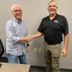 This image shows Ryan from Speedy Buys Homes shaking hands with a homeowner named Steve, marking a successful home closing. Both men appear genuinely happy and satisfied, smiling broadly and displaying warmth and professionalism. Ryan, dressed in a black branded Speedy Buys Homes polo shirt, reinforces the company's professional image and commitment to reliable, friendly service. The handshake symbolizes trust, completion, and mutual satisfaction, effectively highlighting Speedy Buys Homes' dedi