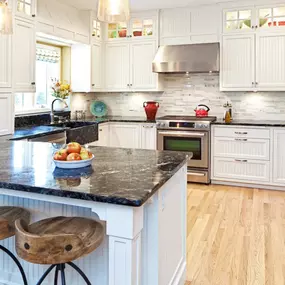 A modern kitchen features white cabinets, stainless steel appliances, and a dark granite island with stools. Light wood flooring complements the space.