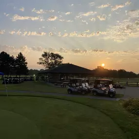 Golf carts lined up and ready for the day at Audubon Golf Course, with a glimpse of the practice putting green and the course in the background.