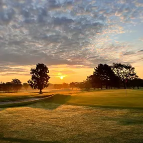 Brilliant orange sunrise over Audubon Golf Course, with the green on the right and trees and fairways in the background.