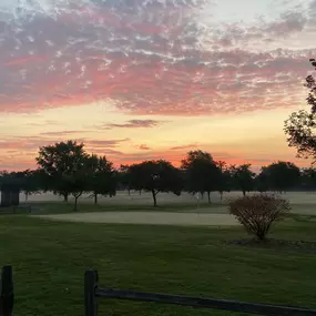 Beautiful sunset at Audubon Golf Course, with a fence in the foreground, green in the middle, and trees silhouetted against the colorful sky.