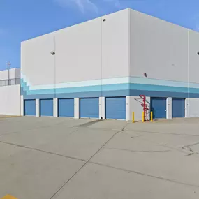 Spencer Street Self Storage drive-up storage units featuring easy-access blue roll-up doors and spacious entry area. The clean exterior showcases our convenient ground-floor units with direct vehicle access for efficient loading and unloading.
