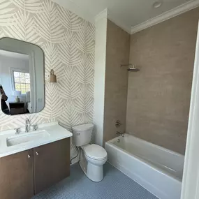 Stylish guest bathroom featuring a bathtub with textured wall tile and a modern vanity with a circular mirror.
