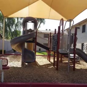 A playground with a yellow canopy and a red slide.