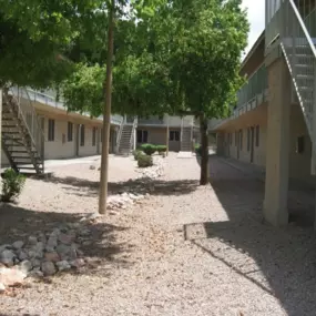 A courtyard with trees, gravel, and stairs leading to buildings.