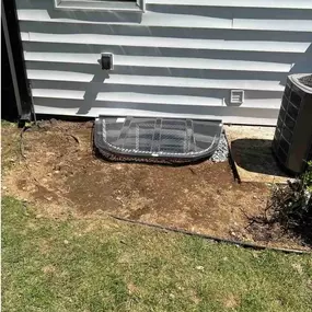 This image showcases a newly installed flat-top window well cover by Egress of Long Island, designed to provide essential safety and protection for basement egress systems. The transparent polycarbonate cover features a low-profile, semi-circular design that sits flush against the home's white vinyl siding, creating a clean, professional appearance.  The cover is engineered with a hinged design and reinforced construction to support weight while still allowing for quick emergency exit when neede