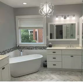 This bathroom features agreeable gray walls, a white vanity with a marble top, and a freestanding tub. The floor has a light-colored herringbone tile, complemented by a mosaic accent tile on the wall.