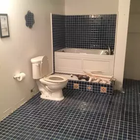 This bathroom features a white toilet and bathtub with a tiled surround. Dark blue square tiles cover the floor and extend up the shower walls, while decorative yellow and blue tiles adorn the bathtub's base.