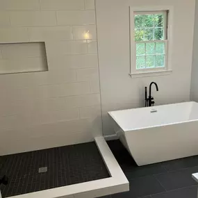 This modern bathroom showcases a spacious walk-in shower with white subway tiles and a dark tiled floor. Adjacent to it, a sleek white freestanding tub with a matte black faucet sits on matching dark floor tiles.
