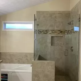 This bathroom features a knee wall walk-in shower with beige tiles and a frameless glass door. A bathtub is adjacent to the shower, and a small window provides natural light.