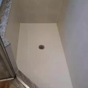 This image showcases a clean, low-curb shower with light beige square tiles and pristine white grout, highlighting the expertise of Grout Specialists. The shower floor is visible with a central drain, emphasizing cleanliness.