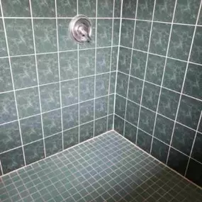 This image showcases a shower corner restored by The Groutsmith, featuring deep green wall tiles and matching small floor tiles. Clean, bright grout lines emphasize the expert tile rejuvenation work performed.