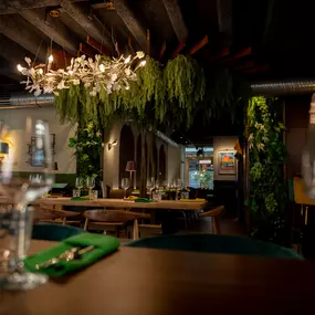 Stilvoll eingerichteter Restaurantbereich mit Holzbalkendecke, Kronleuchtern und üppiger Pflanzen-Dekoration – einladendes Ambiente mit moderner Eleganz.