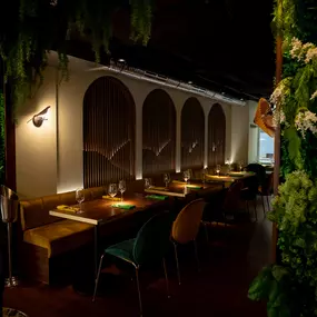 Stimmungsvoll beleuchteter Restaurantbereich mit eleganten Sitznischen, warmem Licht und üppiger grüner Wandgestaltung – ideal für ein stilvolles Dinner.